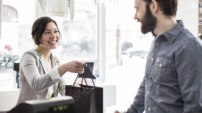 Female design professional giving a shopping bag to customer at cash counter in a studio space. Female design professional giving a shopping bag to customer at cash counter in a studio space.